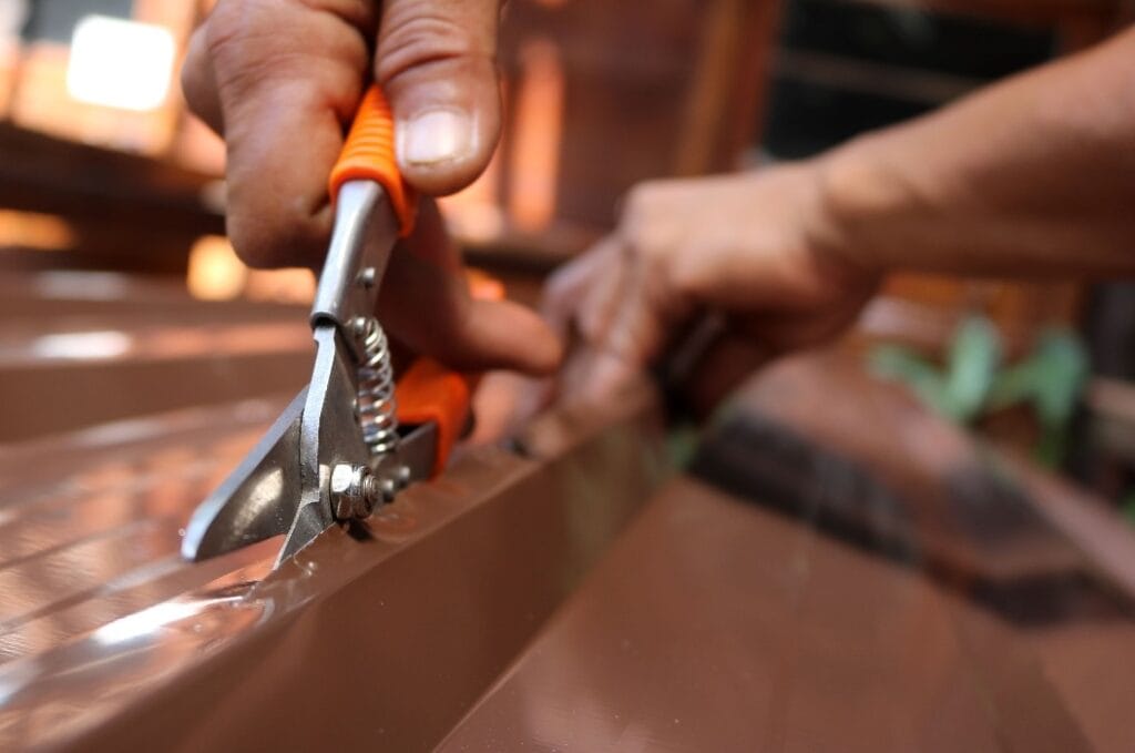Workers use scissors to cut the metal sheet for roofing.
